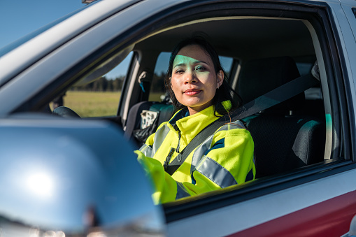 Asian female airfield operations officer sitting in a follow me car on an airport runway. She is wearing reflective clothes.