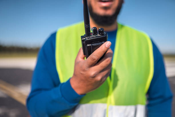 Hispanic airfield operations officer monitoring an airfield. Using a walkie talkie to communicate with an airplane and air traffic control.