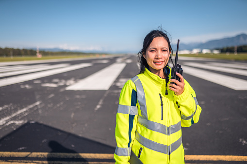 Latin airfield operations officer standing on a runway monitoring an airfield. Using a walkie talkie to communicate with an airplane and an air traffic control.