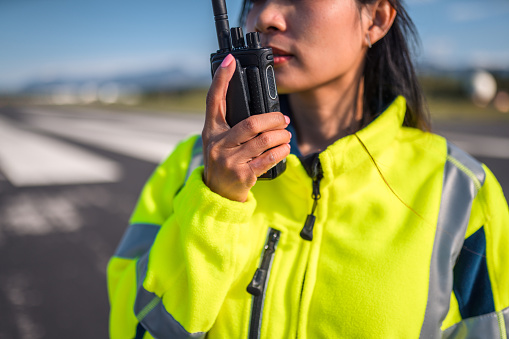 Asian female airfield operations officer monitoring an airfield. Using a walkie talkie to communicate with an airplane and air traffic control.