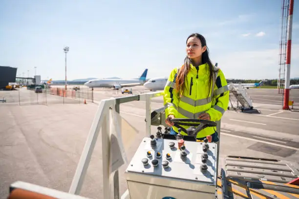 Photo of Asian Female Airport Worker In A Reflective Vest Operating A Container Loader