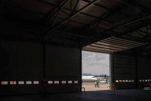 Airport workers standing in front of an open hangar doors. Wearing reflective clothes.
