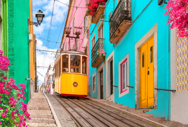 Yellow typical tram in Lisbon, Portugal Yellow typical tram on a street with colorful houses and flowers on the balconies - Bica Elevator going down the hill of Chiado in Lisbon, Portugal. tram stock pictures, royalty-free photos & images