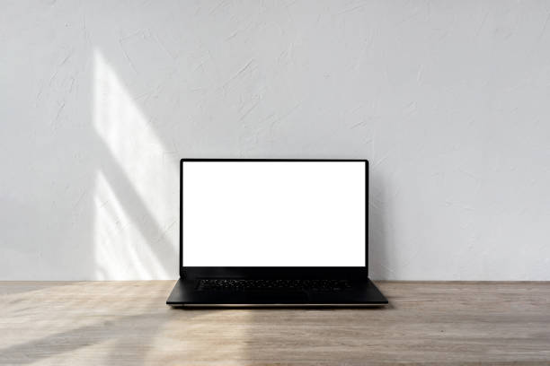 istock Laptop with blank screen mockup on beige wooden table, geometric sunlight shadows on textured white wall, minimalist business, branding template, home interior design background 1483204401