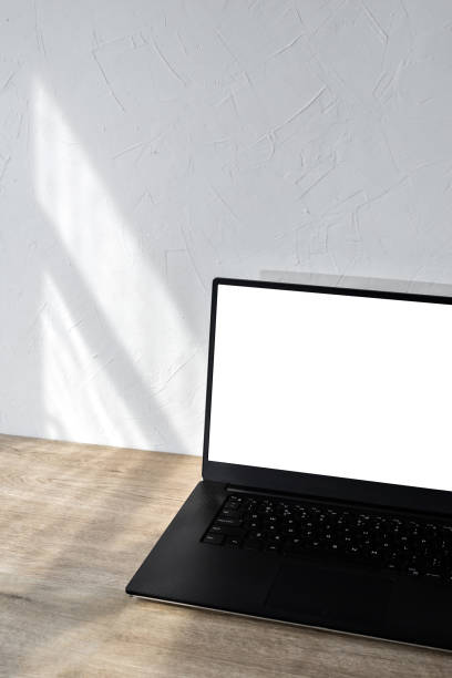 istock laptop with blank screen mockup on beige wooden table, aesthetic sunlight shadows on white wall, minimalist business branding template, background with copy space 1483204624