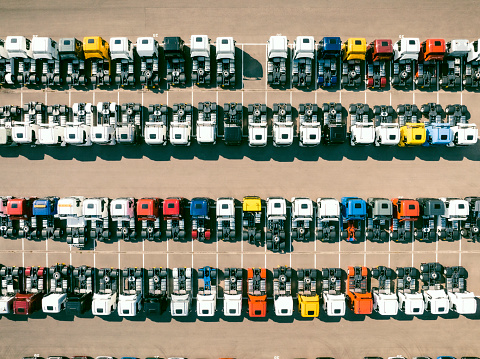 Various different colored trucks in a row at a parking lot seen from above. The trucks are parked next to eachother in neat lines.