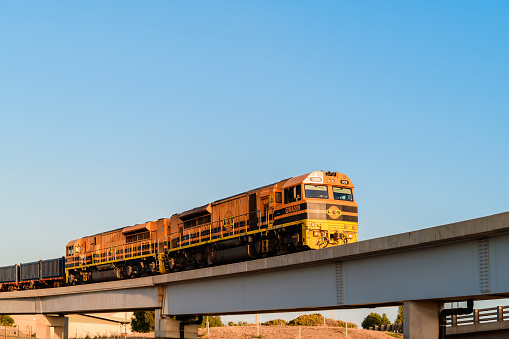 Adelaide, Australia - April 11, 2020: Genesee & Wyoming GWA009 Diesel-Electric operational freight locomotive passing over the Port River at Port Adelaide while lit up by sunset light