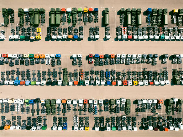 Various different colored trucks in a row at a parking lot seen from above. The trucks are parked next to eachother in neat lines.
