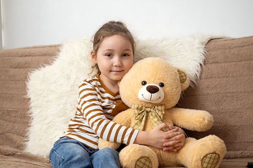 Little cute caucasian girl hugs her favorite toy big teddy bear. Love and tenderness. Happy childhood concept. Gift for a birthday or other holiday