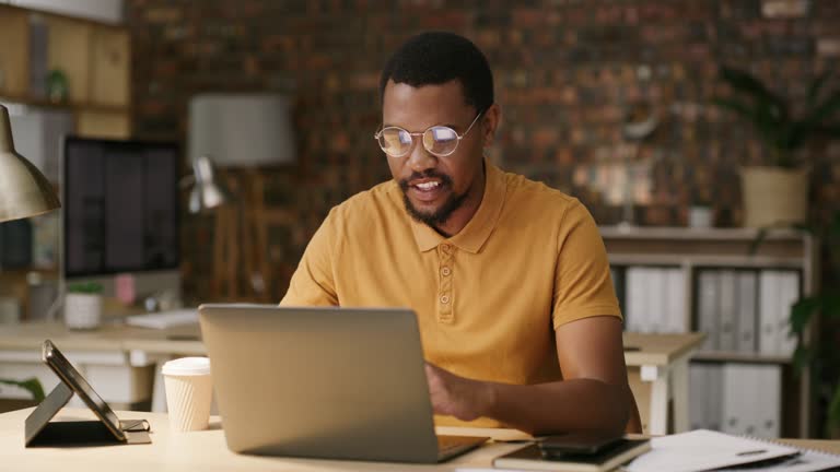 Laptop, night and black man working and typing a project in the evening for overtime work in an office as a freelance worker. Research, employee and happy male planning startup company strategy