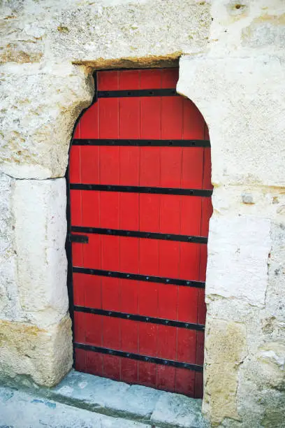 The Medieval red door stands out against the ancient stone walls. The wood is carved with intricate details, creating a mysterious atmosphere.