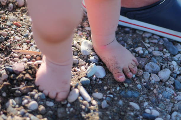 istock Baby son doing first steps on the beach. Bare feet staying on the sand. Summertime holidays concept. Top view 1483215936