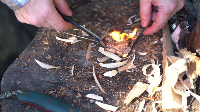 A male tourist man striking fire using knife, flint and birch bark
