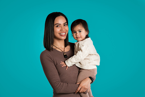 Maori woman and her daughter portrait against blue backdrop in studio, Auckland, New Zealand.