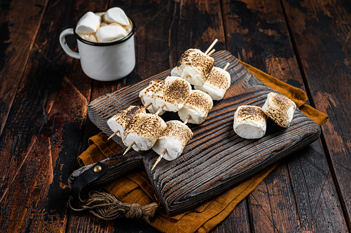 Roasted Marshmallow on the sticks with Cup of coffee on wooden board. Wooden background. Top view