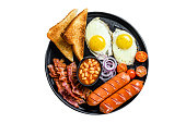 English breakfast with fried eggs, sausages, bacon, beans and toasts in a plate.  Isolated on white background.