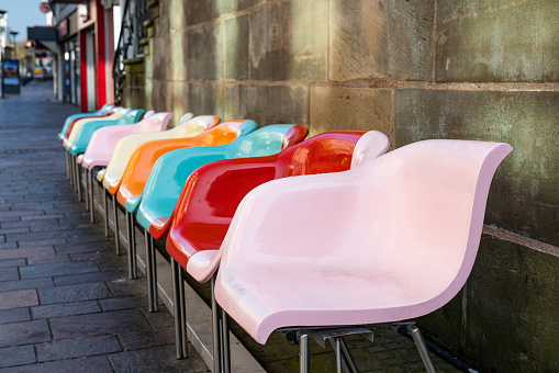 Multi colored plastic seats in the pedestrian area of city against the background of a gray concrete wall.