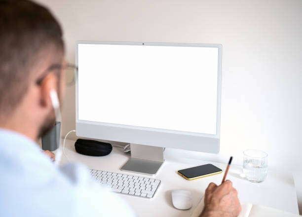 istock Male person sitting at desk looking at computer screen and writing notes with pencil. 1483223203