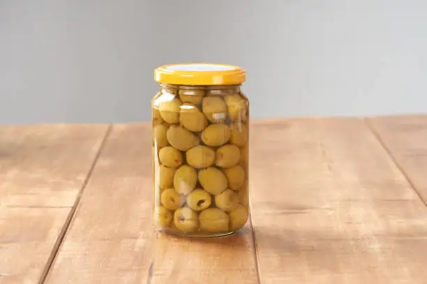 Olives in a glass jar on the wooden table.