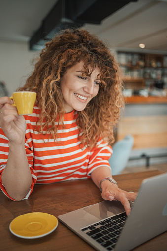 Young beautiful woman sitting in a cafe looking at her laptop, surfing the internet or working online and enjoying a cup of coffee