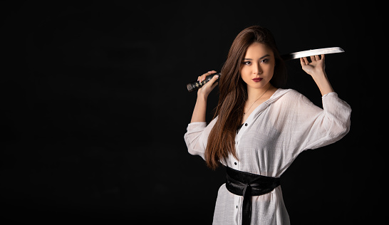 Portrait of asian girl with katana samurai sword on black background with copy space.