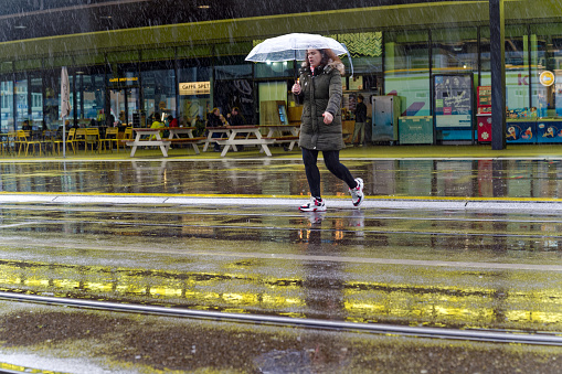 Pedestrian with umbrella crossing road on a rainy spring day at City of Zürich district Oerlikon. Photo taken April 1st, 2023, Zurich, Switzerland.