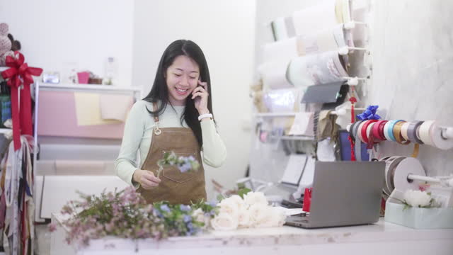 Asian chinese female florist wrapping red roses bouquet at her flower shop counter for customer order