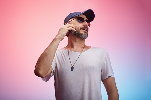 Man wearing casual clothing, t-shirt and a cap using smart phone in front of colorful background