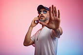 Man making stop gesture while talking to phone and standing against colorful background