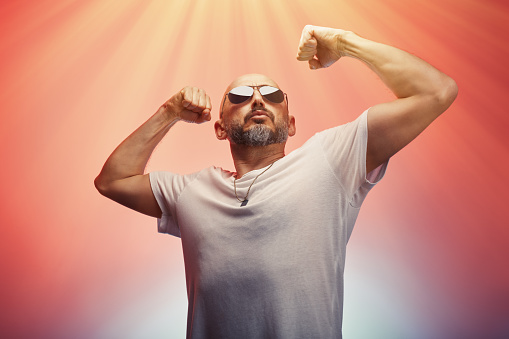 Hombre flexionando los músculos de sus brazos y bíceps mostrando su fuerza y poder masculino, fondo colorido photo