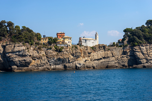 Rocky Coast of the famous Portofino village with the church of Saint George. Luxury tourist resort in Genoa Province, Liguria, Italy, Europe. Mediterranean sea (Ligurian sea).