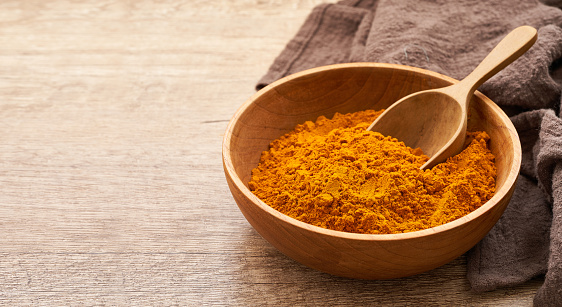 close up a pile of ground turmeric powder or curcumin powder in wood plate and scoop on wooden table background. turmeric or curcumin powder