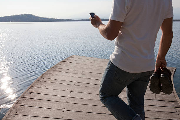 istock Man walking along a wooden jetty, checking phone 148323169