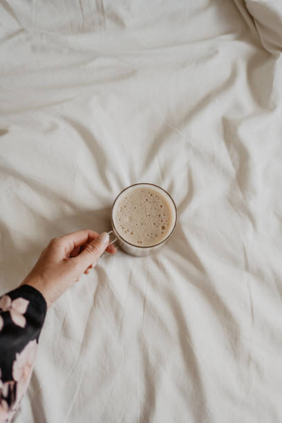 istock Female hand holding a cup of capuccino coffee on white bed with copy space 1483233253