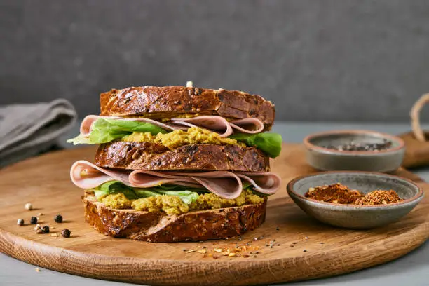 Healthy sandwich for breakfast, with ham, homemade curry sauce and green salad, served on a wooden home, bar or restaurant table with a  pepper and chili pepper, close up image with a copy space, macro hero view image