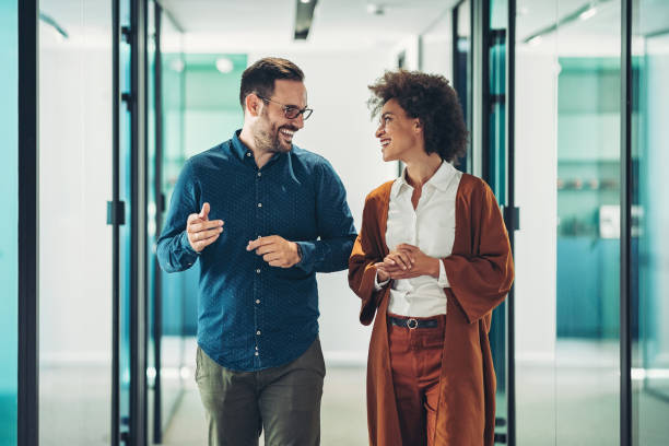 Couple of business persons walking together and talking Smiling business persons having a conversation colleague stock pictures, royalty-free photos & images