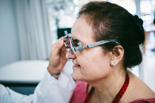 A young female optometrist checks the eyesight of an adult woman with a trial frame