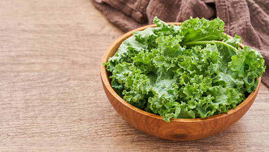 fresh green Kale leaves bunch leaf cabbage in wood plate or bowl on wooden table background. green kale or leaf cabbage