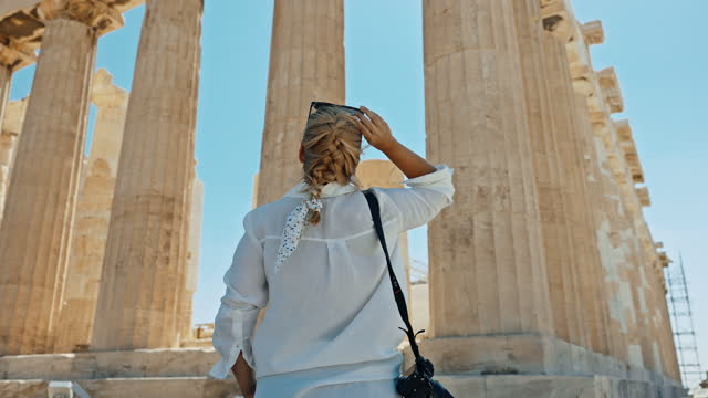 Blond female tourist looking at Parthenon temple during vacation. Rear view of blond female tourist standing with camera looking at Parthenon temple at Acropolis of Athens,Greece during vacation. Acropolis of Athens,Greece