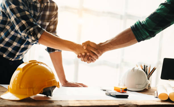 istock Construction team shake hands greeting start new project plan behind yellow helmet on desk in office to consults about their building project.. 1483235474