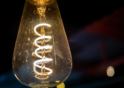 LED (Light Emitting Diode) filament bulb - close-up view of individual illuminated spiral filament and other interior components. Frequently used as energy-saving warm mood lighting.