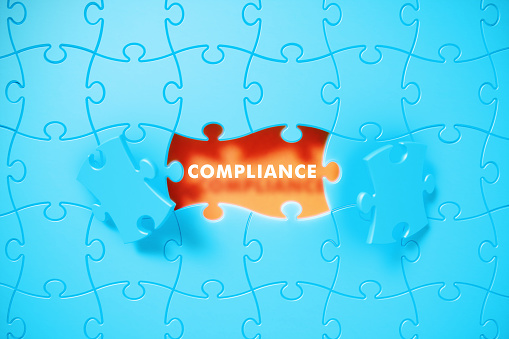 Blue jigsaw puzzle pieces revealing compliance word on orange background. Horizontal composition with copy space. Compliance concept.