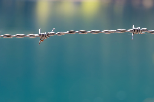 Blurred background with macro close up of pointed sharp steel metal barbed wire as concept for prison prohibited border control migration borders confinement cordoned off areas