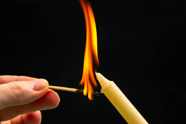 istock Lighting a candle with a wooden match on a dark background. Burning candle fire 1483241979