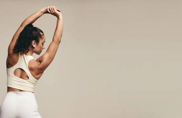 Sporty young female working out with muscle-toning stretch exercises in a studio. Athletic young woman striving for better flexibility and balance through regular strength training.