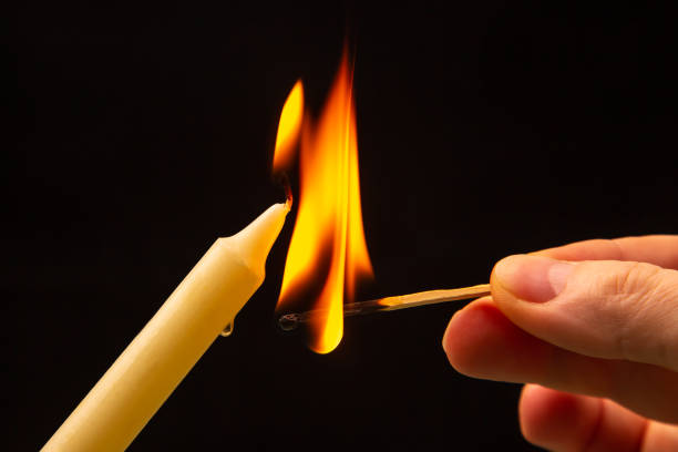 istock Lighting a candle with a wooden match on a dark background. Burning candle fire 1483242422