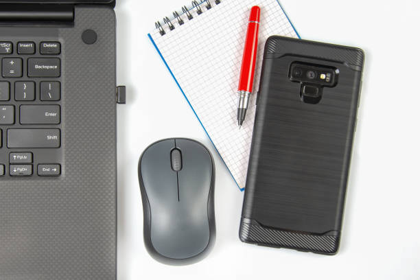 istock Computer wireless mouse, pen and notepad next to a laptop on a white table close-up. Items for office work 1483242990