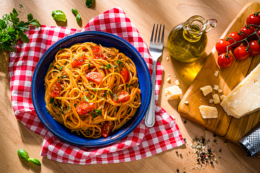Italian pasta plate shot from above on wooden table. The composition includes parmesan cheese and grater, extra virgin olive oil bottle, tomatoes, salt and pepper, basil and parsley among others. High resolution 42Mp studio digital capture taken with SONY A7rII and Zeiss Batis 40mm F2.0 CF lens