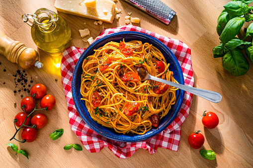 Italian pasta plate shot from above on wooden table. The composition includes parmesan cheese and grater, extra virgin olive oil bottle, tomatoes, salt and pepper, basil and parsley among others. High resolution 42Mp studio digital capture taken with SONY A7rII and Zeiss Batis 40mm F2.0 CF lens