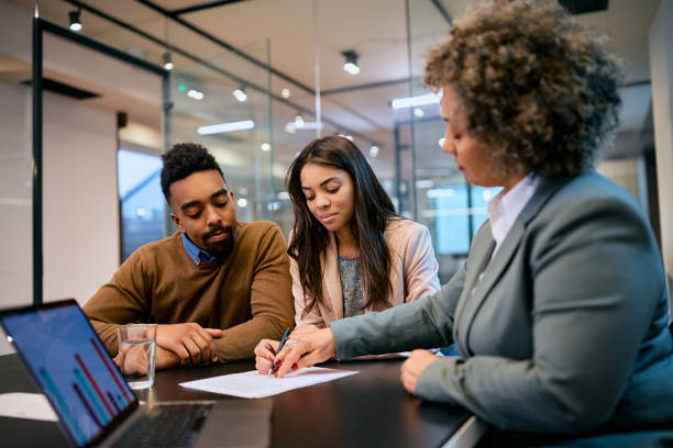 Young black couple signing a contract with insurance agent in the office. African American woman and her husband signing mortgage agreement during a meeting with their bank manager. mortgage document stock pictures, royalty-free photos & images